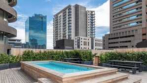 A rooftop pool with wooden steps, surrounded by greenery and modern buildings in the background. - One Thibault Residence By Itc Hospitality (Cape Town)