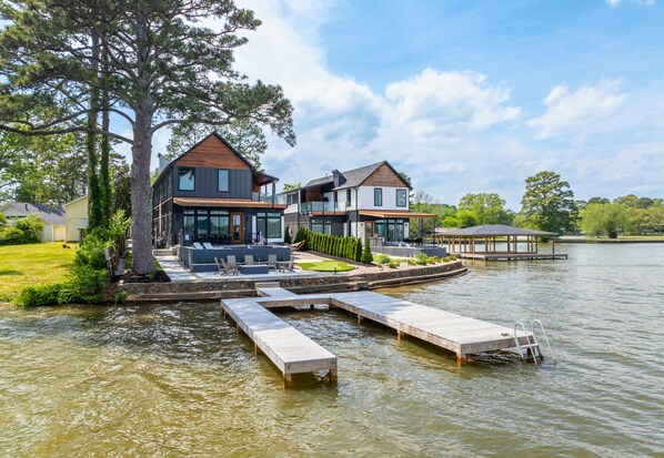 A lakeside property with two modern houses, a dock, and a grassy area.