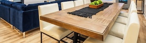 A long wooden dining table with a black macrame runner, surrounded by white chairs.