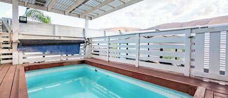 Una piscina interior con cubierta de madera, barandillas blancas y una zona techada con techo metálico.