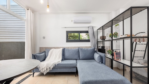Ein modernes Wohnzimmer mit einem grauen Ecksofa, einem Esstisch und einer schwarzen Metallregal mit Pflanzen.