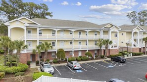 A multi-story hotel with a yellow facade, white balconies, and a parking lot with marked handicapped spaces.