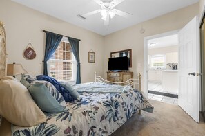 A bedroom with a bed, a television, a dresser, and a door leading to a kitchen.