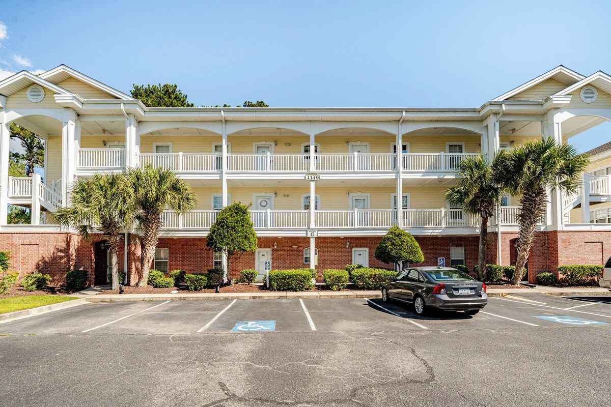 A multi-story hotel with a central courtyard, parking lot, and a car parked in the lot.