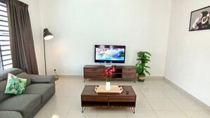 A modern living room with a grey sofa, a coffee table with a vase of flowers, a TV on a wooden stand, and a potted plant. - Tropical Livings Meru Ipoh Homestay (Ipoh)