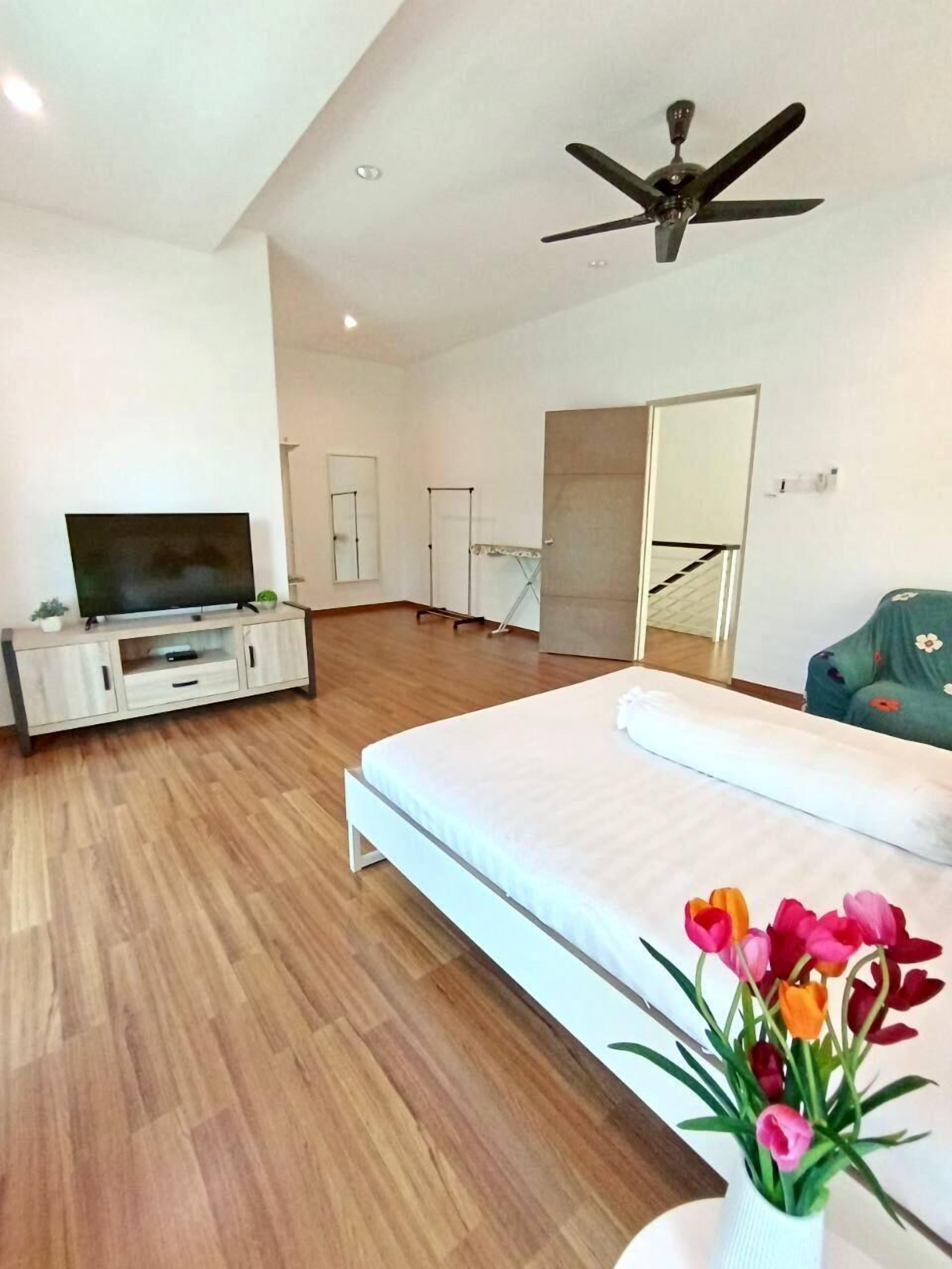 Een ruime kamer met een groot bed, een flatscreen televisie op een witte kast, een plafondventilator en een spiegel.