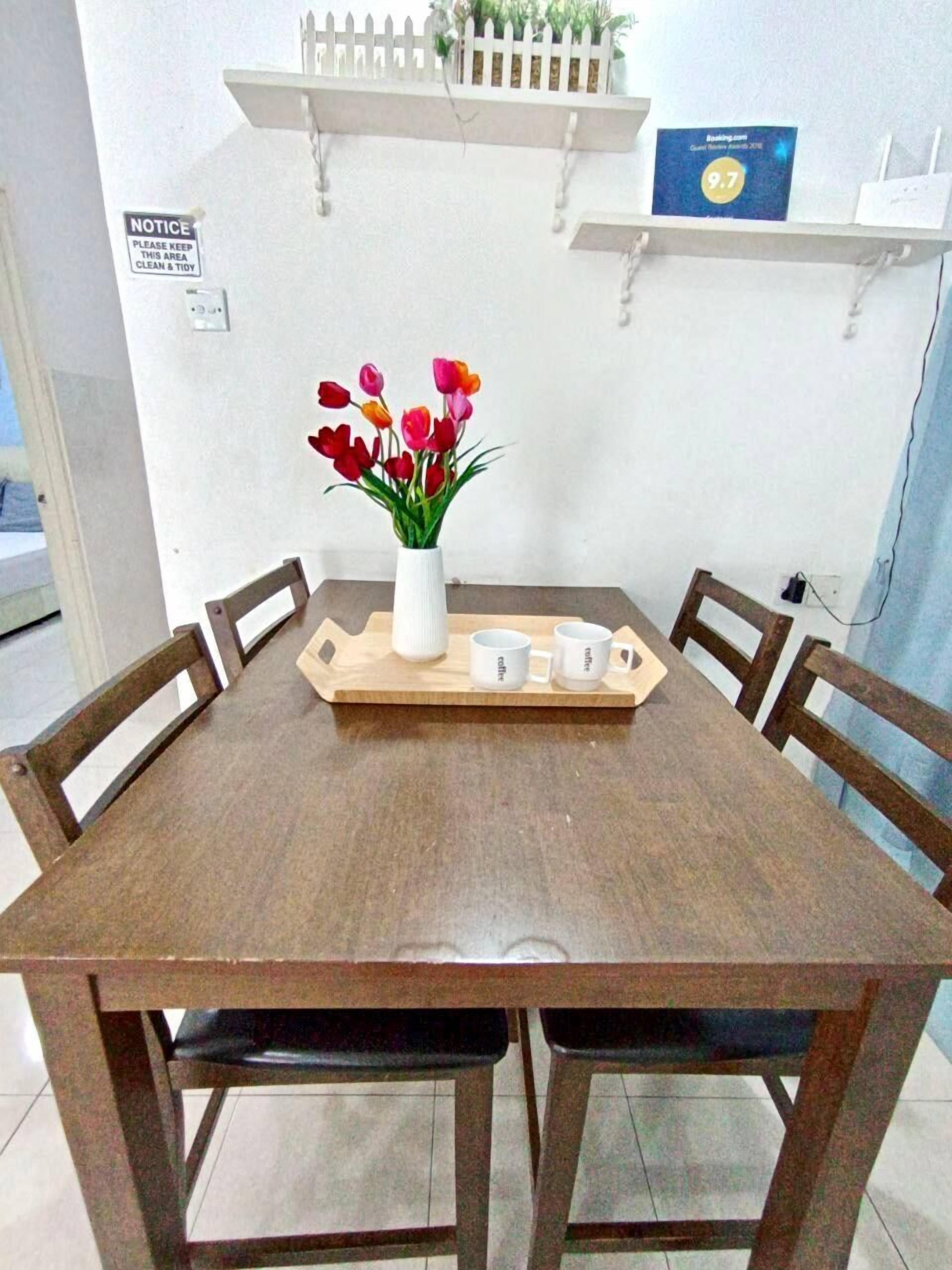 A dining area with a wooden table, four chairs, a white vase with flowers, and a tray with coffee cups.