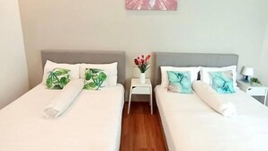 A hotel room with two beds, a ceiling fan, a small table with a vase, and a painting on the wall. - Tropical Livings Meru Ipoh Homestay (Ipoh)