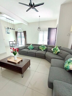A modern living room with a sectional sofa, a coffee table, and a ceiling fan. - Tropical Livings Meru Ipoh Homestay (Ipoh)
