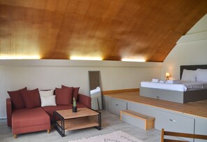 Ein modernes Schlafzimmer im Loft-Stil mit Holzboden, einem roten Sofa, einem Holztisch, einem Bett mit Nachttisch und einem kleinen Schreibtisch.