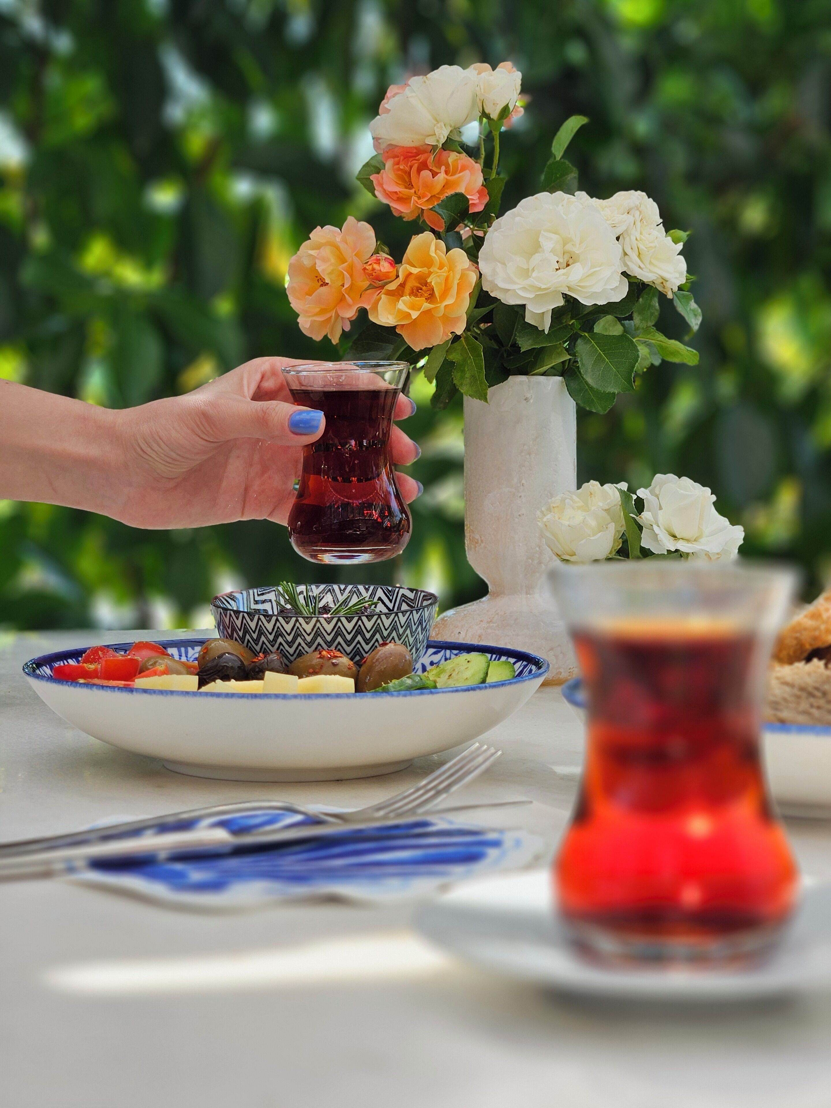 Una mesa con un plato de comida, un tazón, un vaso de líquido rojo y un florero con flores.