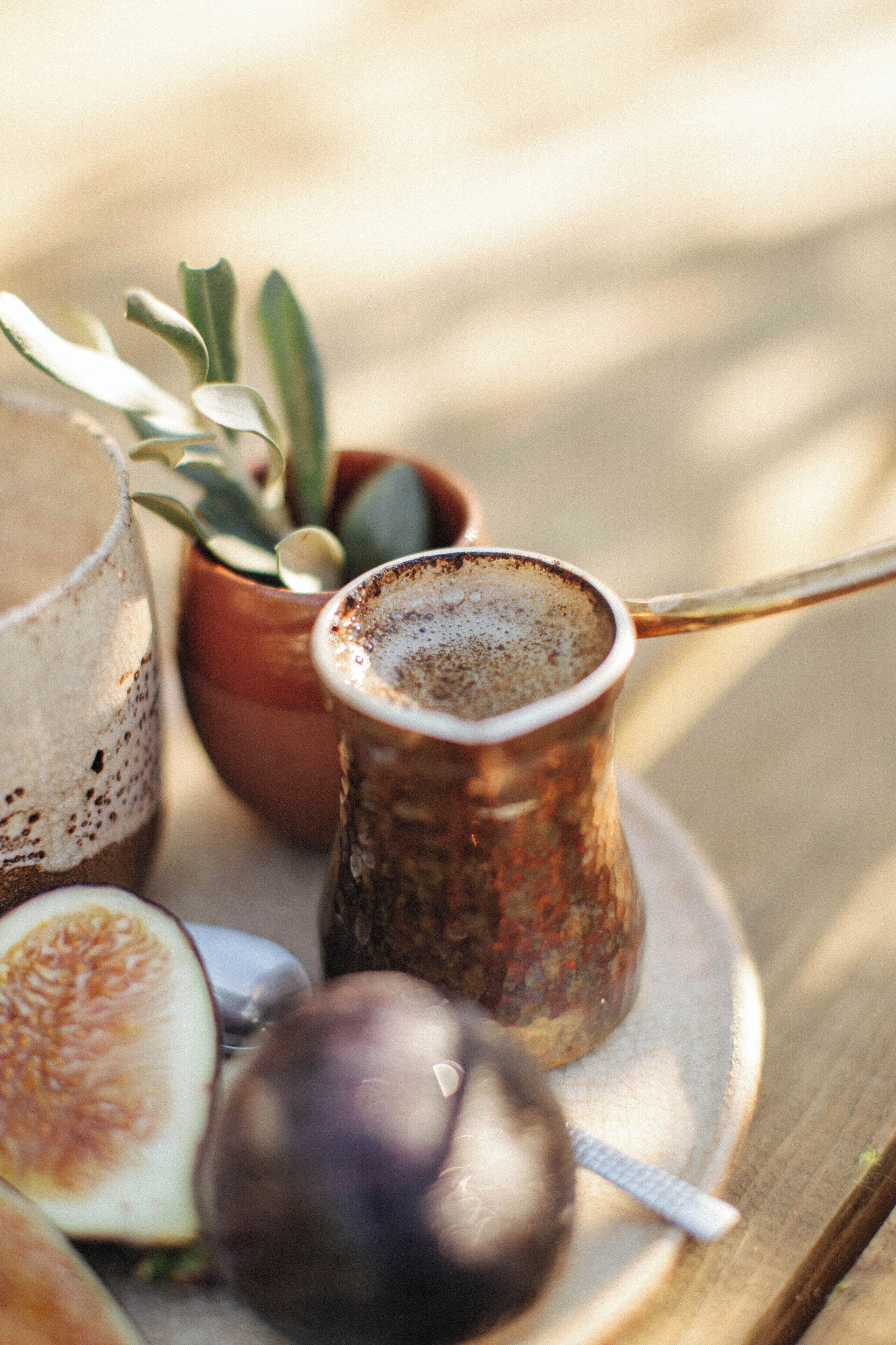 A rustic table setting with a copper cup, a half-cut fig, and a potted plant.
