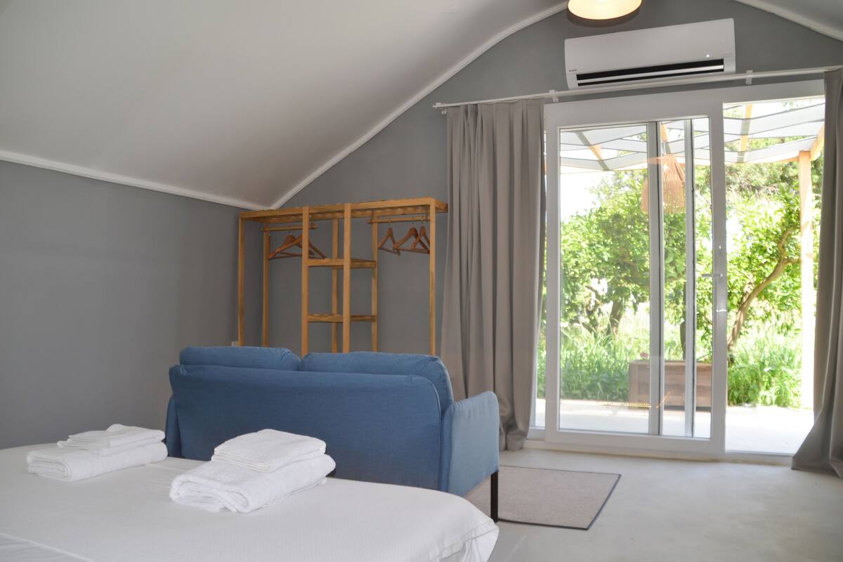 Ein Schlafzimmer mit einem Bett, einem blauen Sofa, einem Holzschrank und einer Glastür, die auf einen Balkon führt.