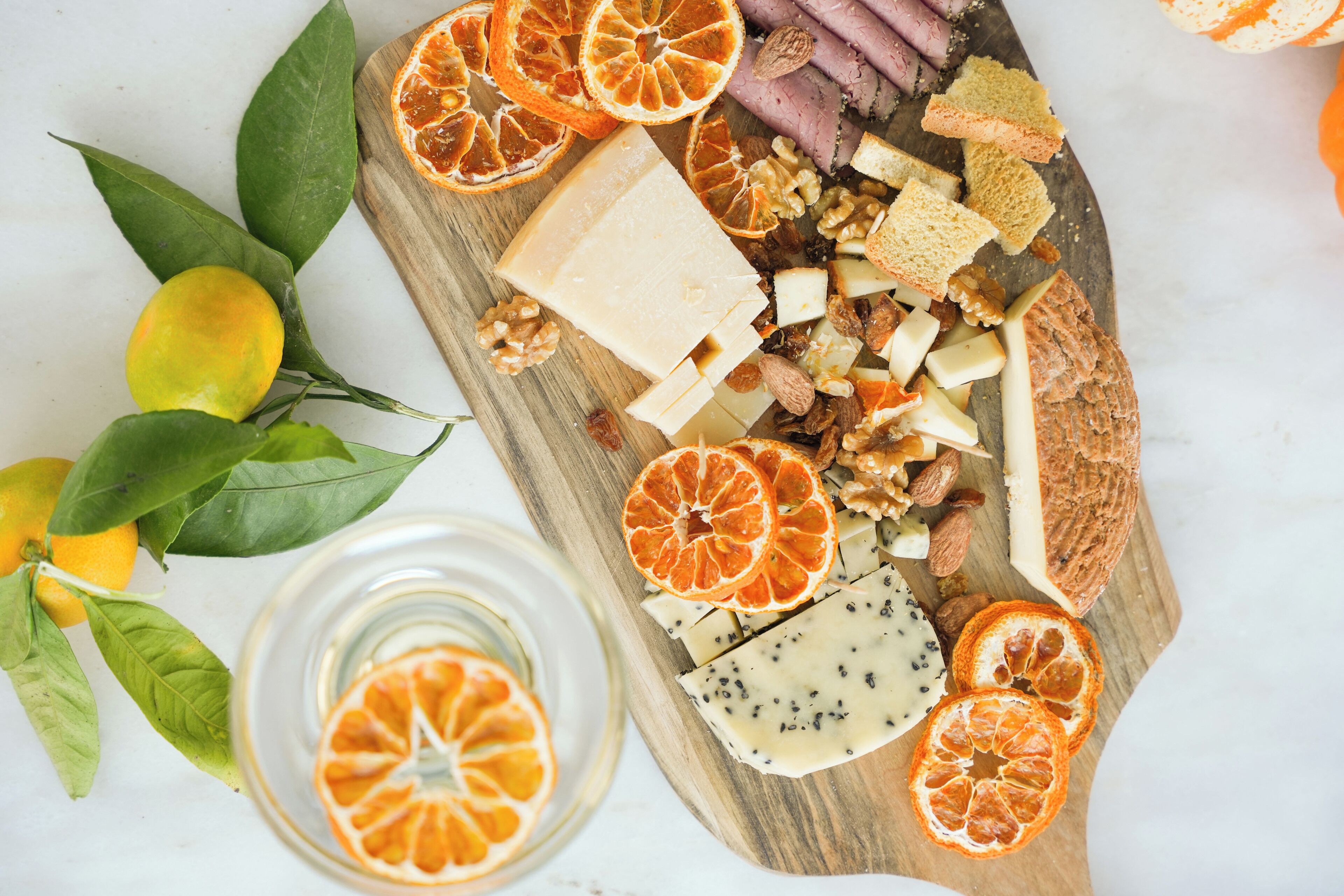 A wooden board with various cheeses, nuts, and dried fruits.