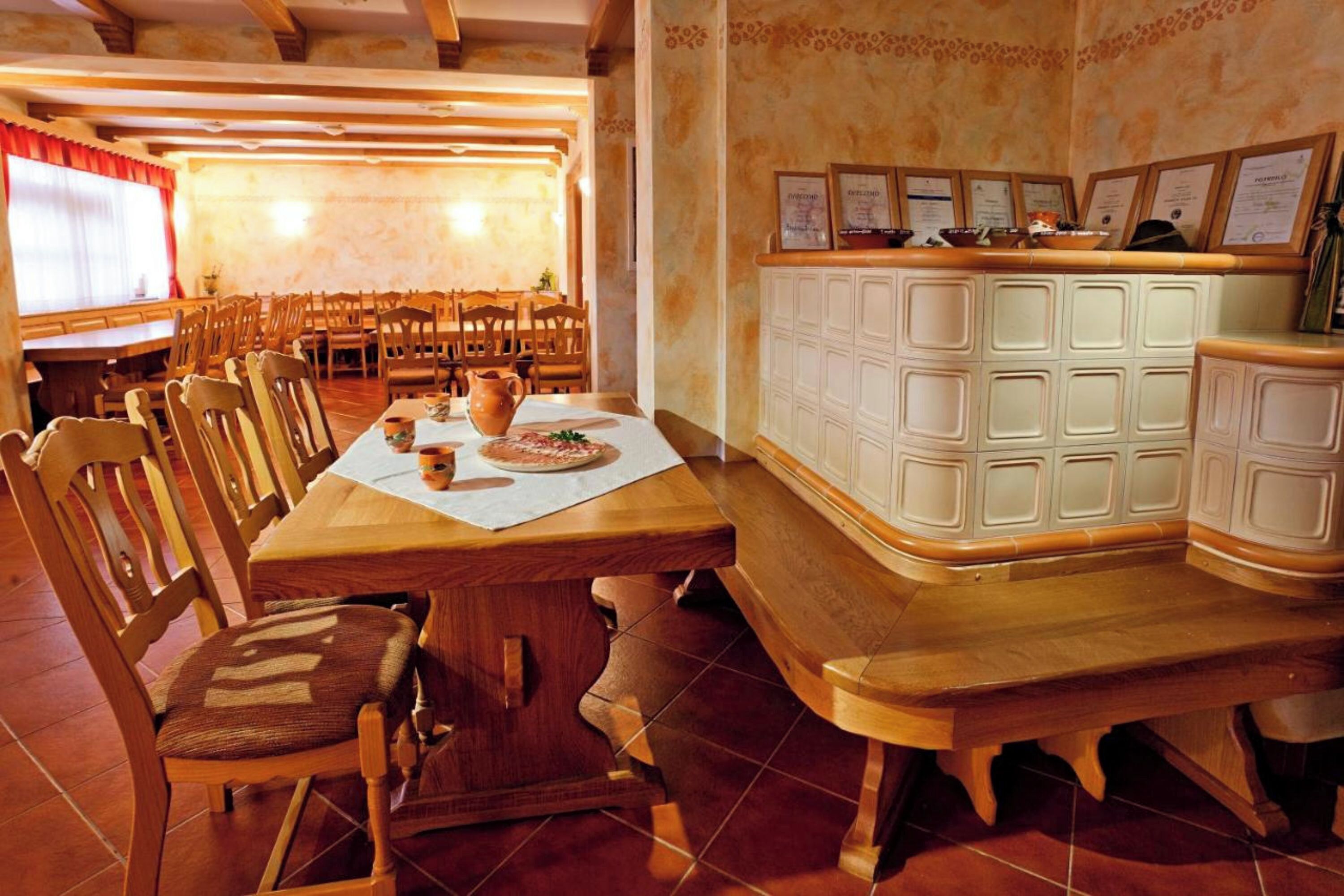 Uma área de refeições com mesas e cadeiras de madeira, um balcão de buffet com alimentos e certificados emoldurados na parede.
