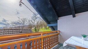 A balcony with a wooden railing, a small table with a plant, and a tiled roof in the background. - Tourist Farm Skrbina Apartment 2 (Smarjeske Toplice)