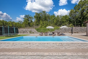 A swimming pool with lounge chairs and umbrellas, surrounded by stone walls and greenery. - Holiday Home Asteria (Labin)