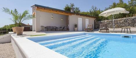 Un espace piscine extérieur moderne, agrémenté d’un mur en pierre, de chaises longues et d’une pergola.