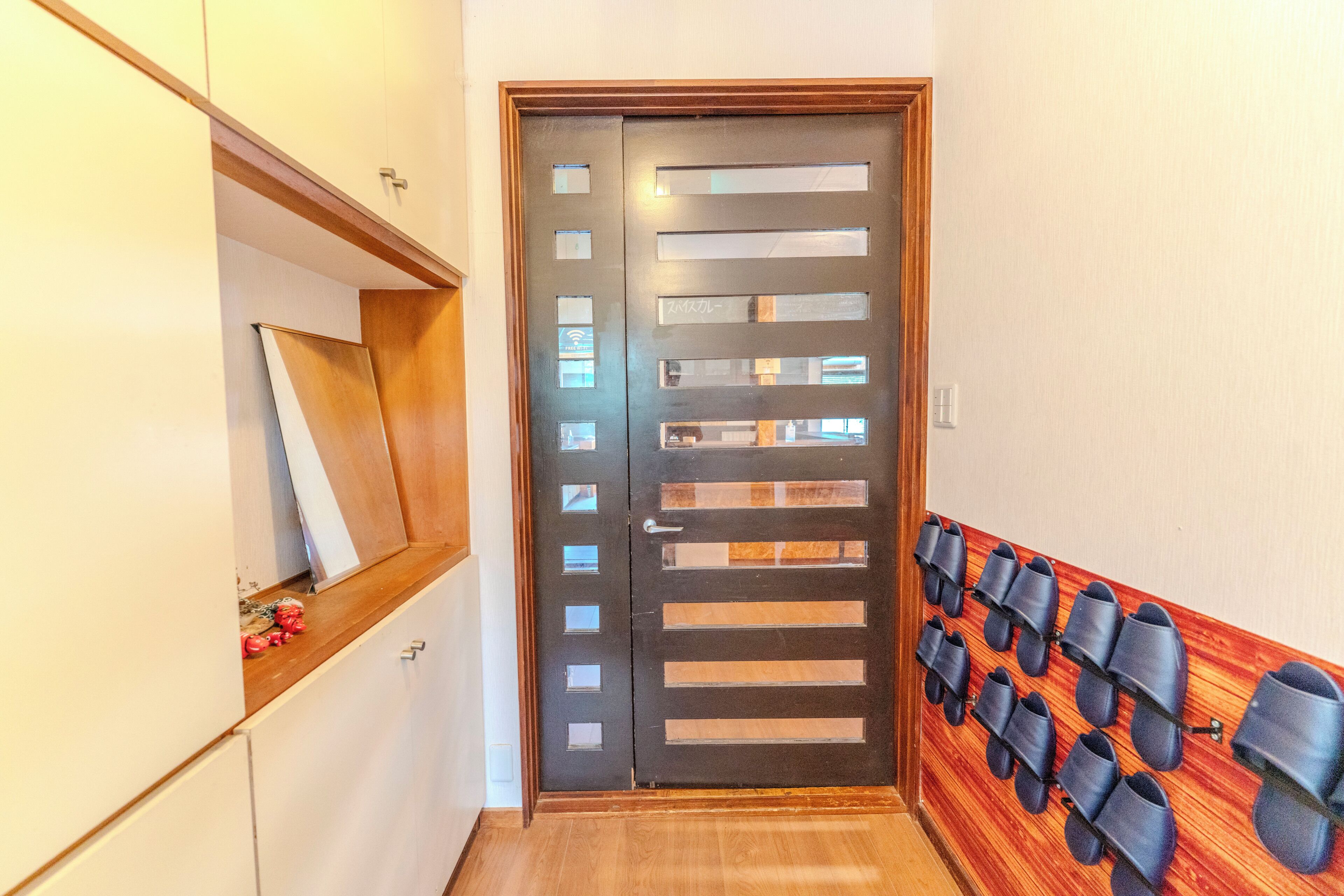 A hallway with a wooden door, a shoe rack, and a white wall.