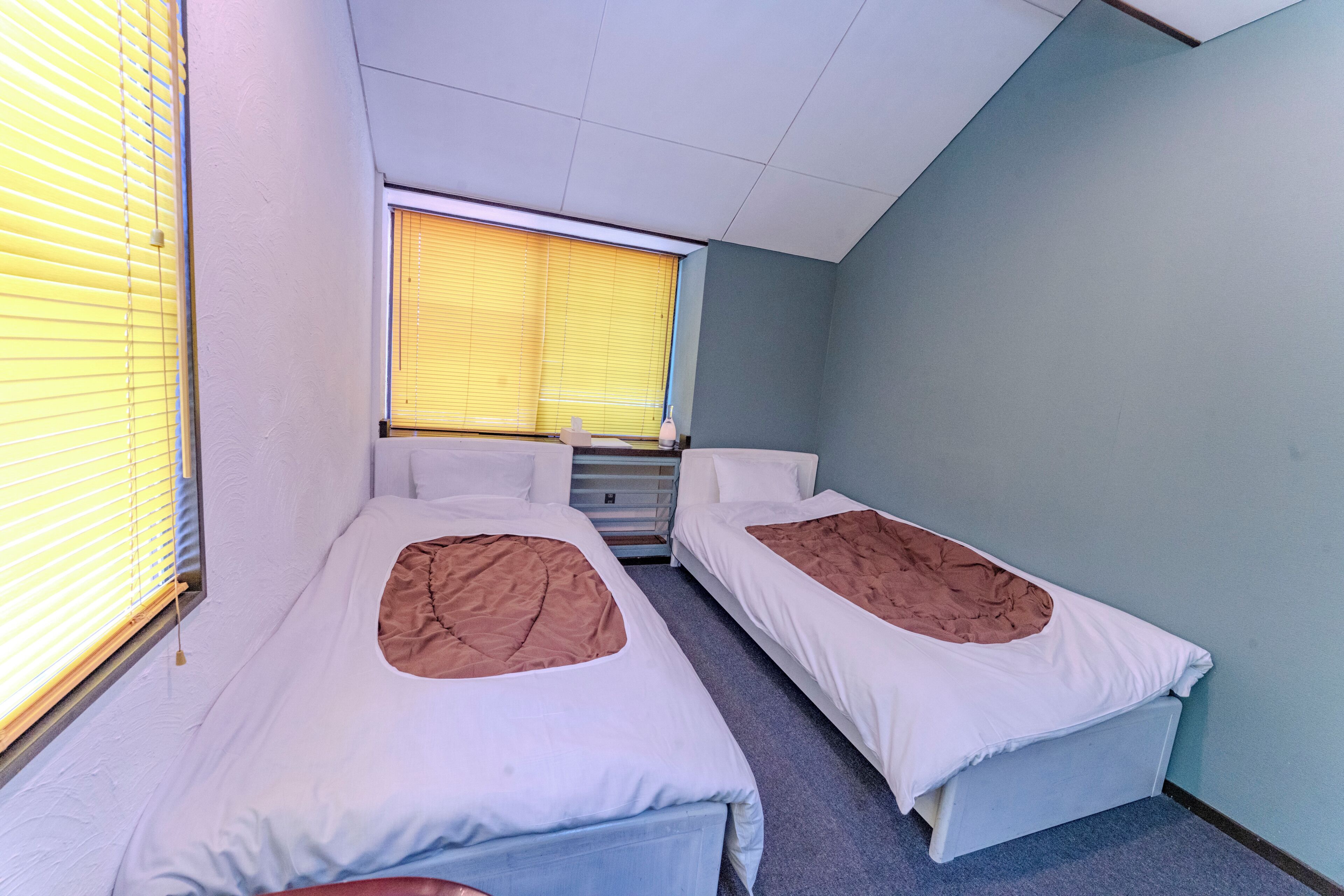 A room with two beds, a window with blinds, and a radiator.