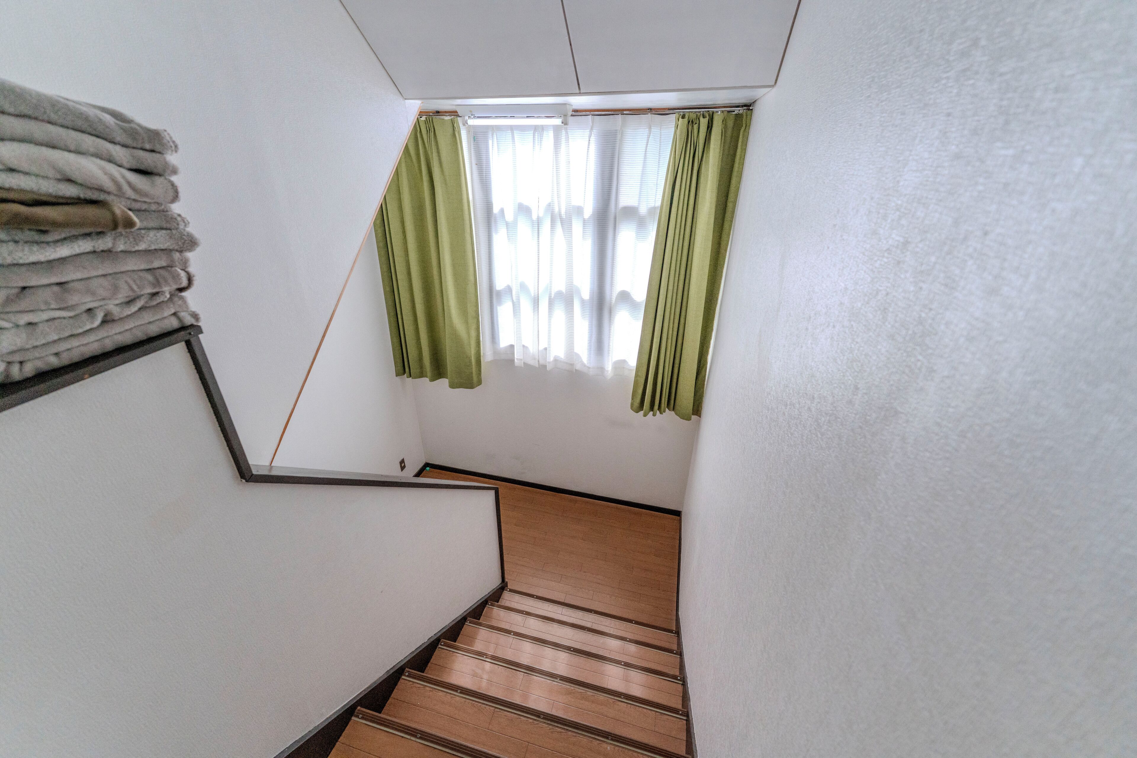 A staircase with wooden steps leading to a room with a window and green curtains.