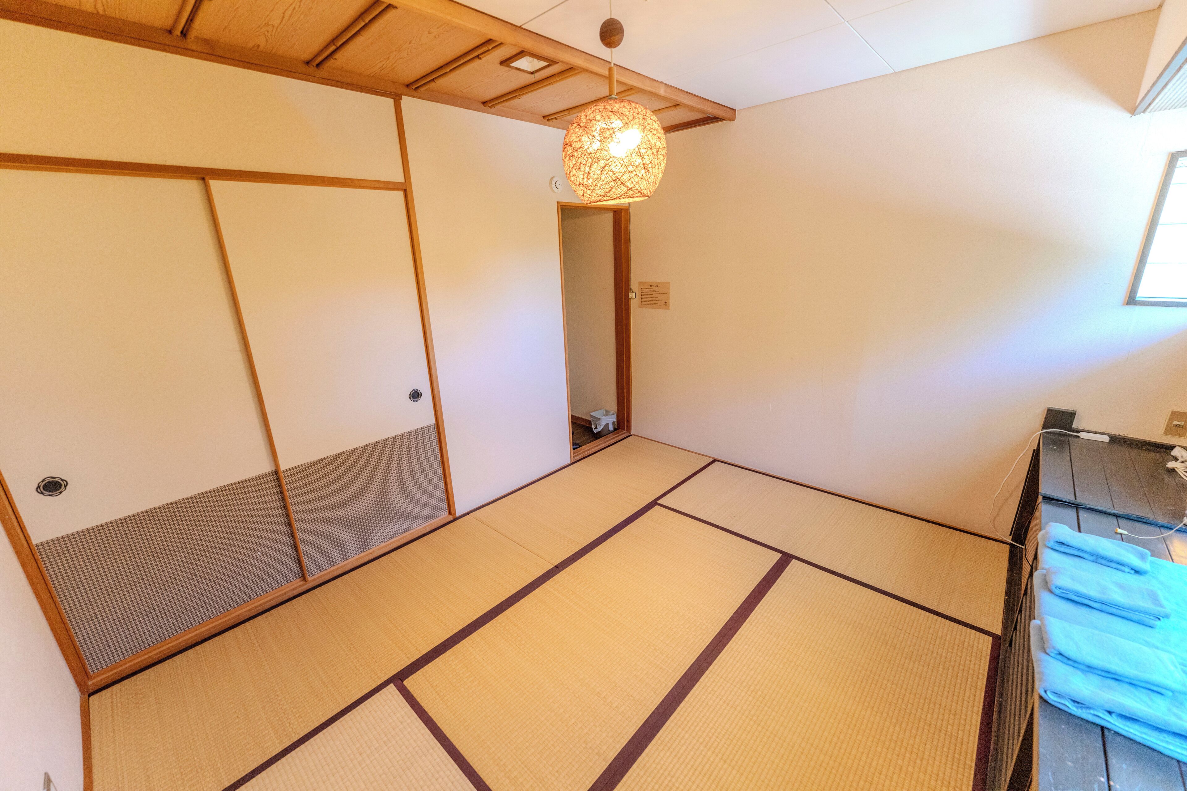 A tatami mat room with a shoji screen door, a hanging light fixture, and a small stool.