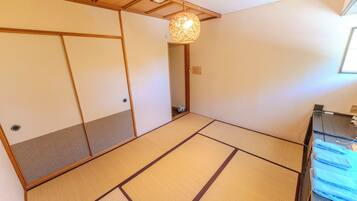 A tatami mat room with a shoji screen door, a hanging light fixture, and a small stool.