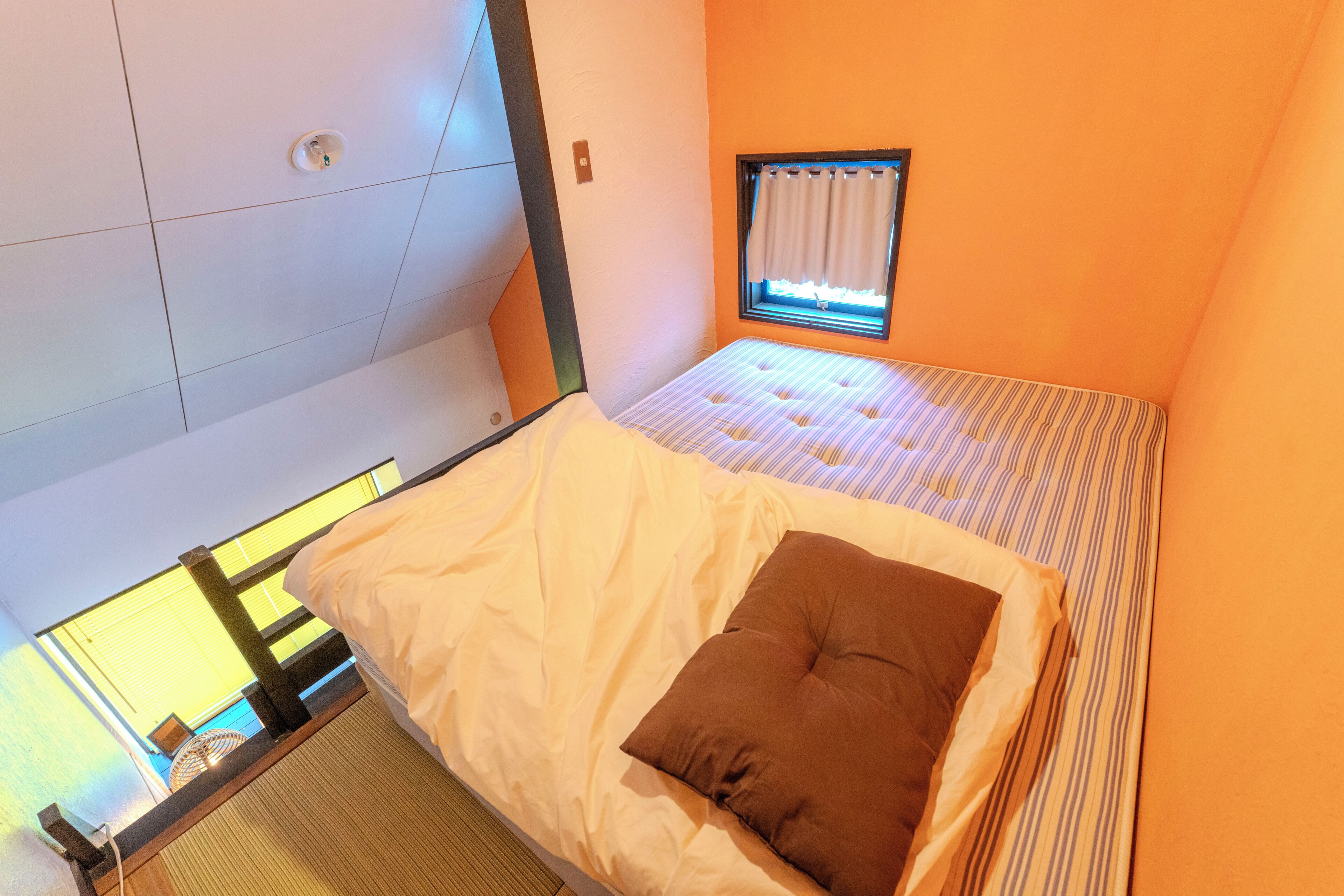 Une pièce comprenant un lit, une fenêtre avec des rideaux et un luminaire fixé au mur.