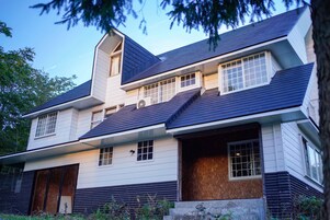 Una casa moderna de dos pisos con techo inclinado, ventanas grandes y una chimenea visible.