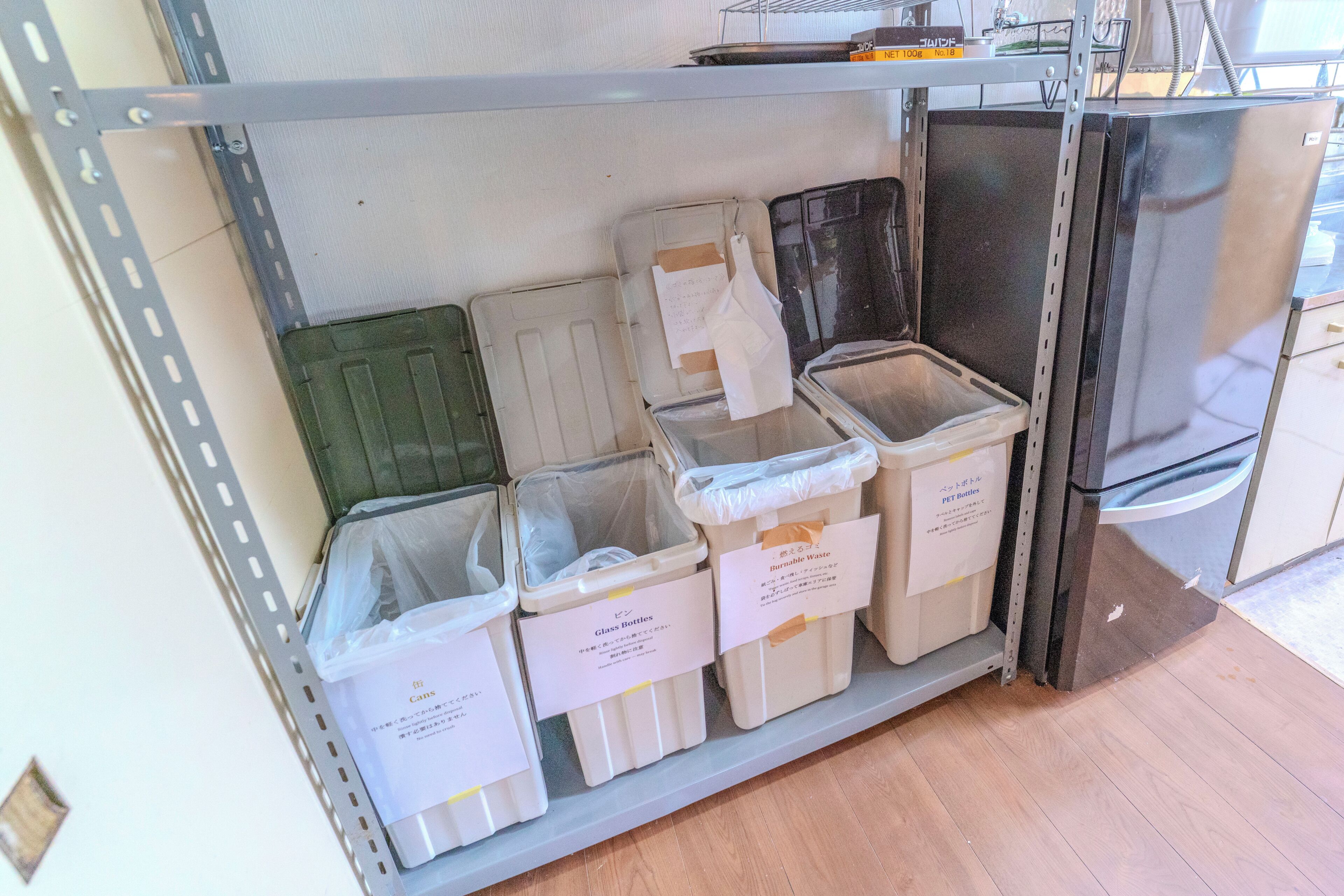 Uma área de armazenamento com contentores identificados para garrafas de vidro, latas e resíduos inflamáveis.
