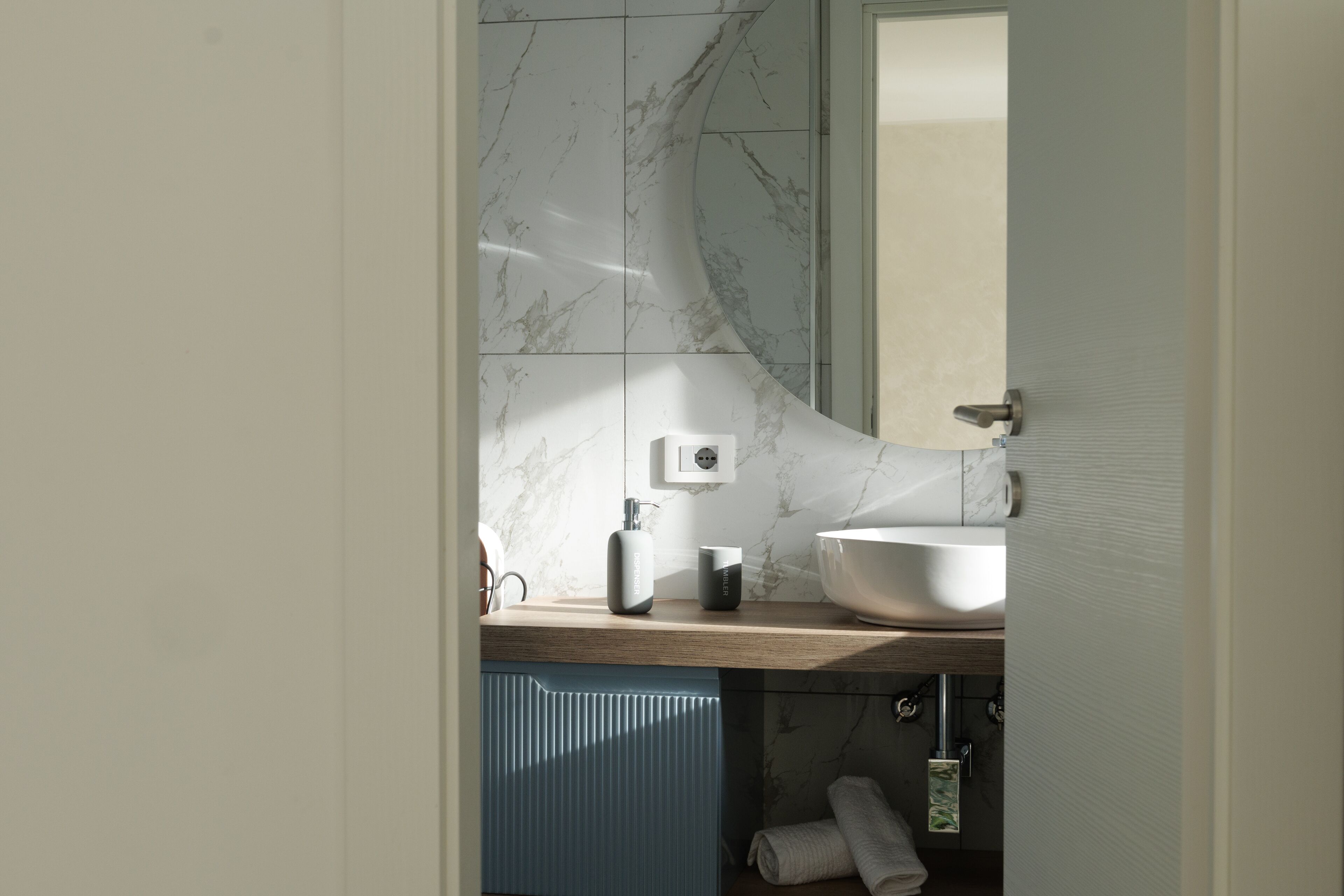 A modern bathroom with a marble backsplash, a large white sink, and a blue cabinet.