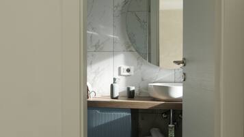 A modern bathroom with a marble backsplash, a large white sink, and a blue cabinet.