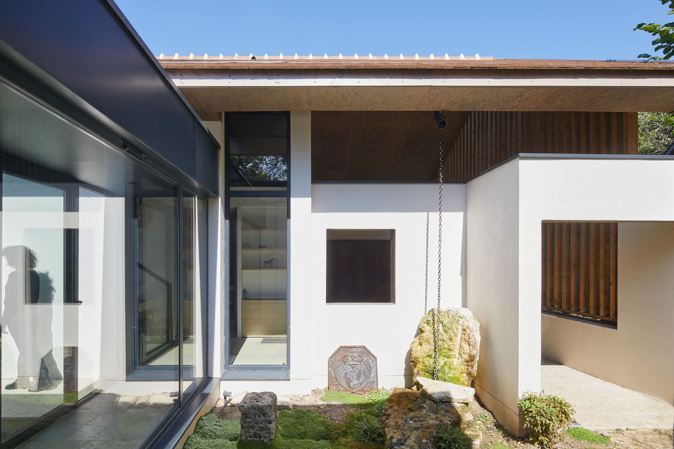 Una casa moderna con puerta de vidrio, una escultura de piedra y un pequeño jardín.