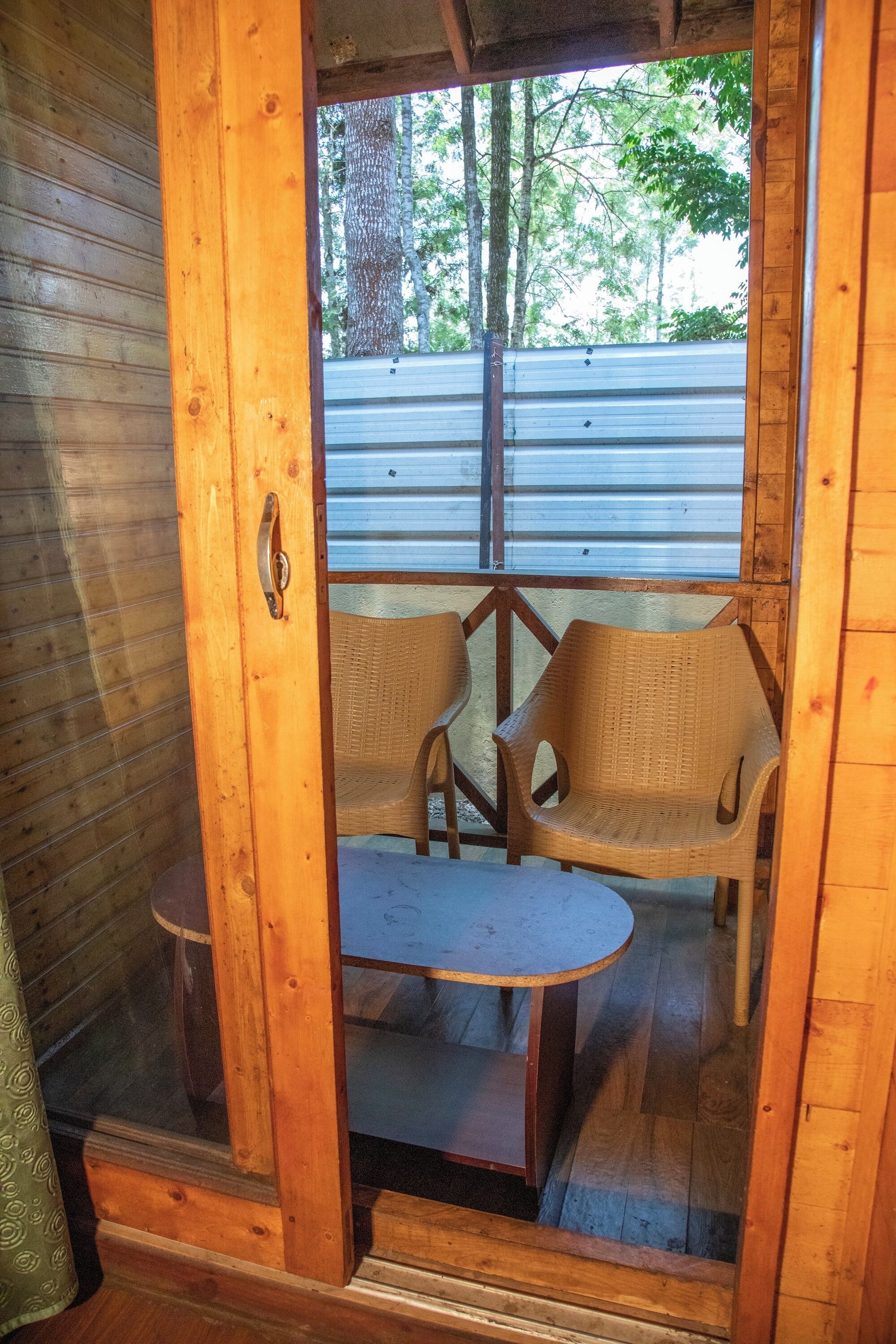 A wooden room with a glass door leading to an outdoor area with wicker furniture and a metal roof.