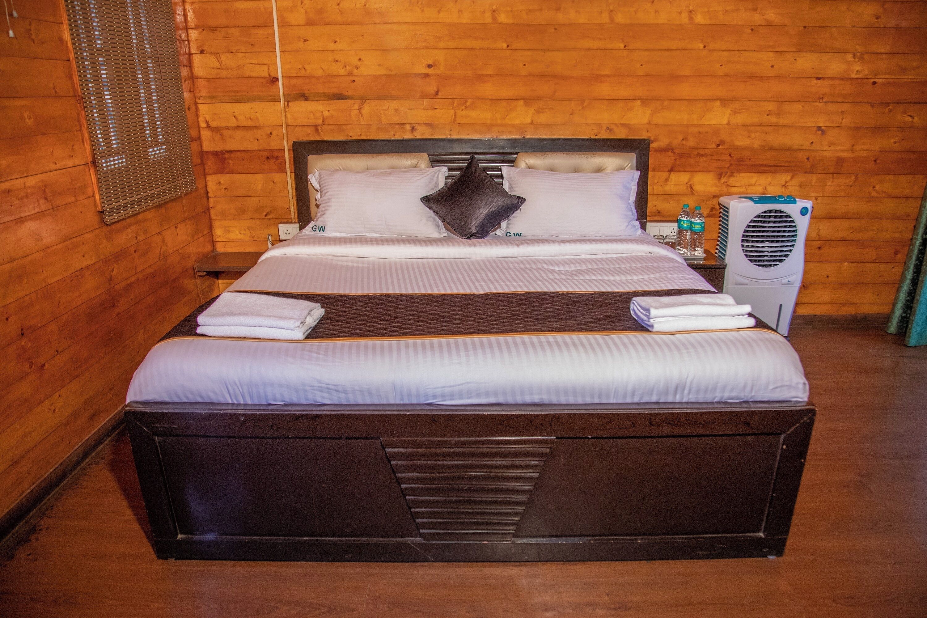 A wooden-paneled room with a large bed, a bedside table, and a wall-mounted air conditioner.
