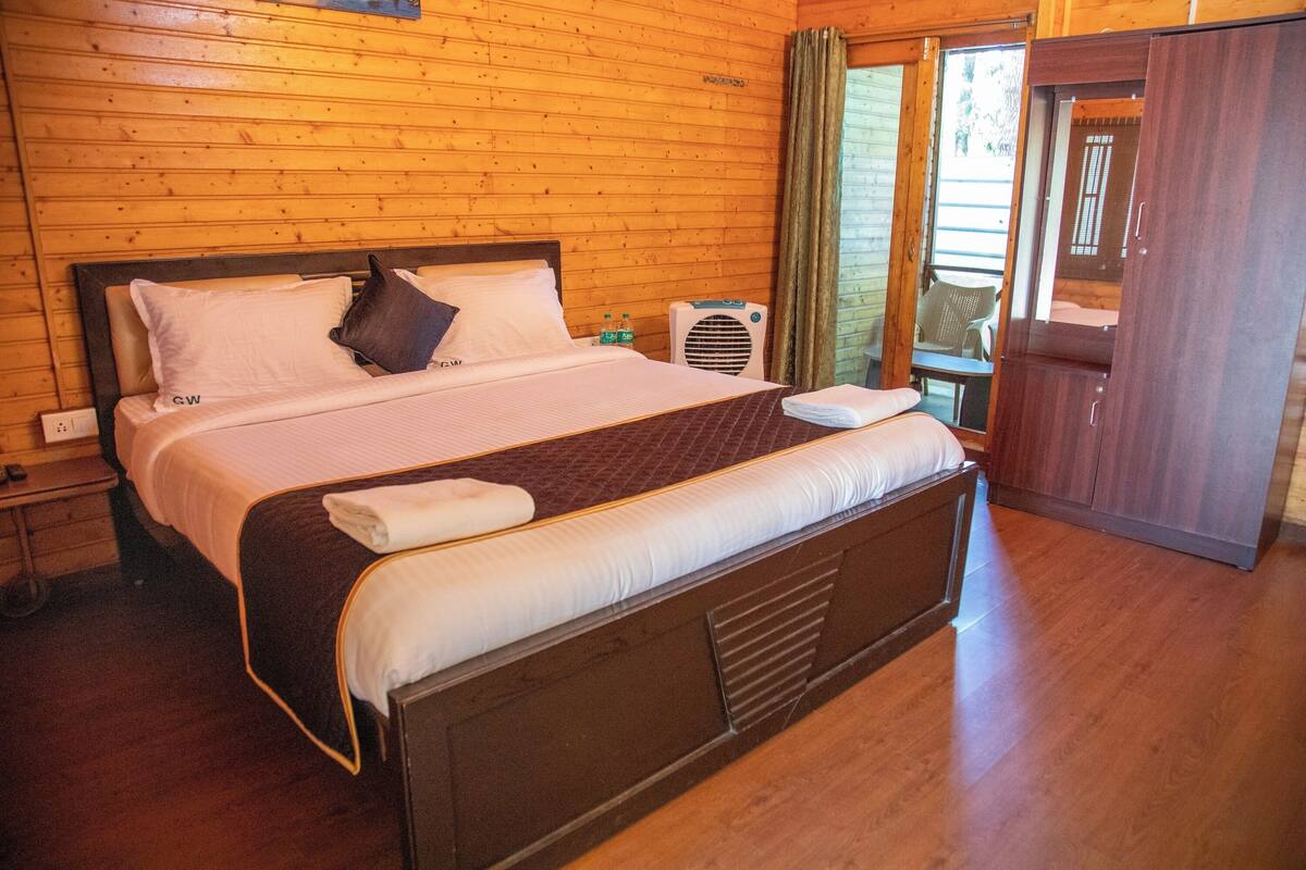 A wooden-paneled bedroom with a large bed, a bedside table, a wardrobe, and a window with curtains.
