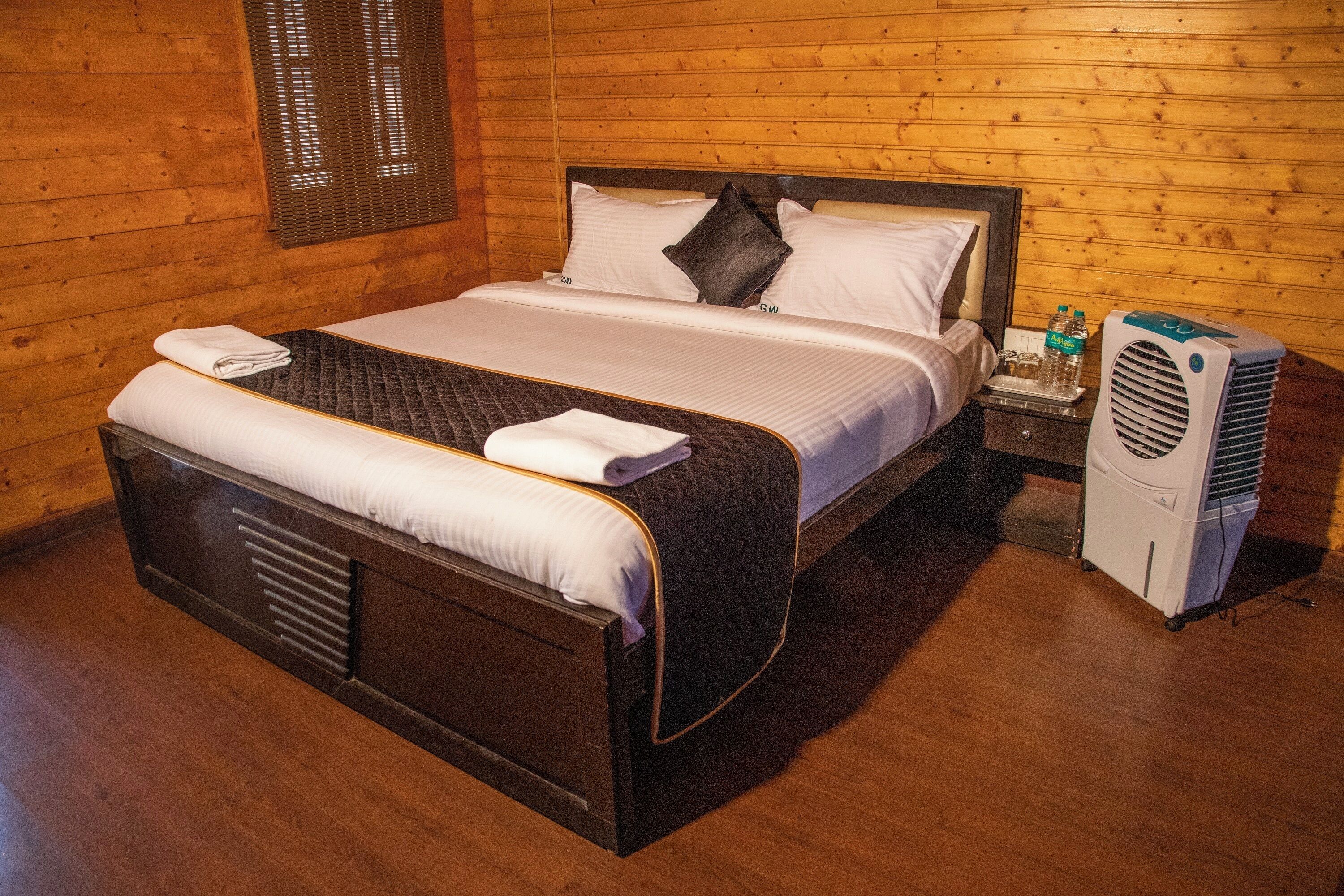 A wooden-paneled room with a bed, a nightstand, and a portable air conditioner.
