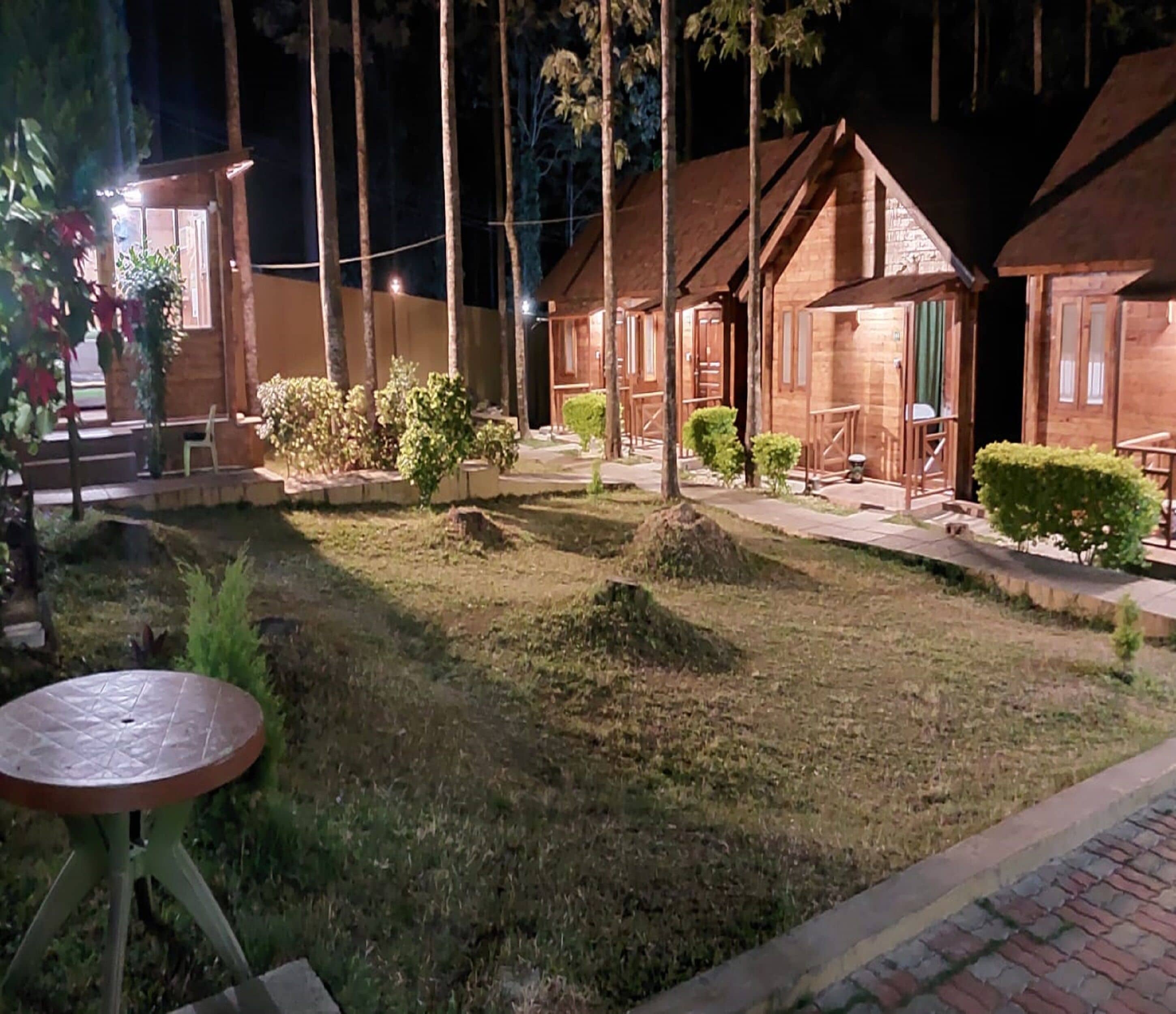 A row of wooden cabins with a grassy lawn and a table in the foreground.