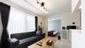 A modern living room with a sofa, a coffee table, and a kitchen area with a microwave. - SERENADE Chitose MS103 (Chitose)