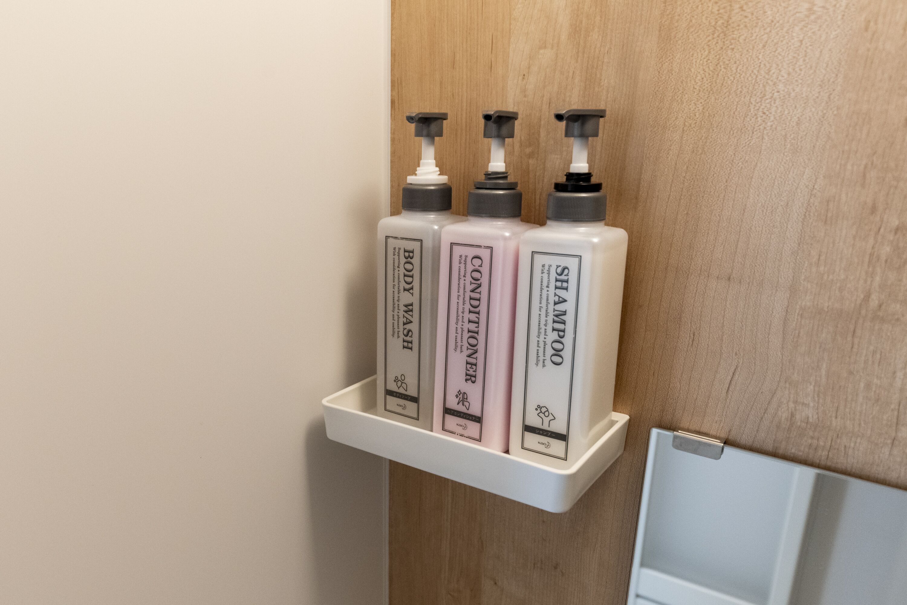 A bathroom shelf with three bottles of body wash, conditioner, and shampoo.