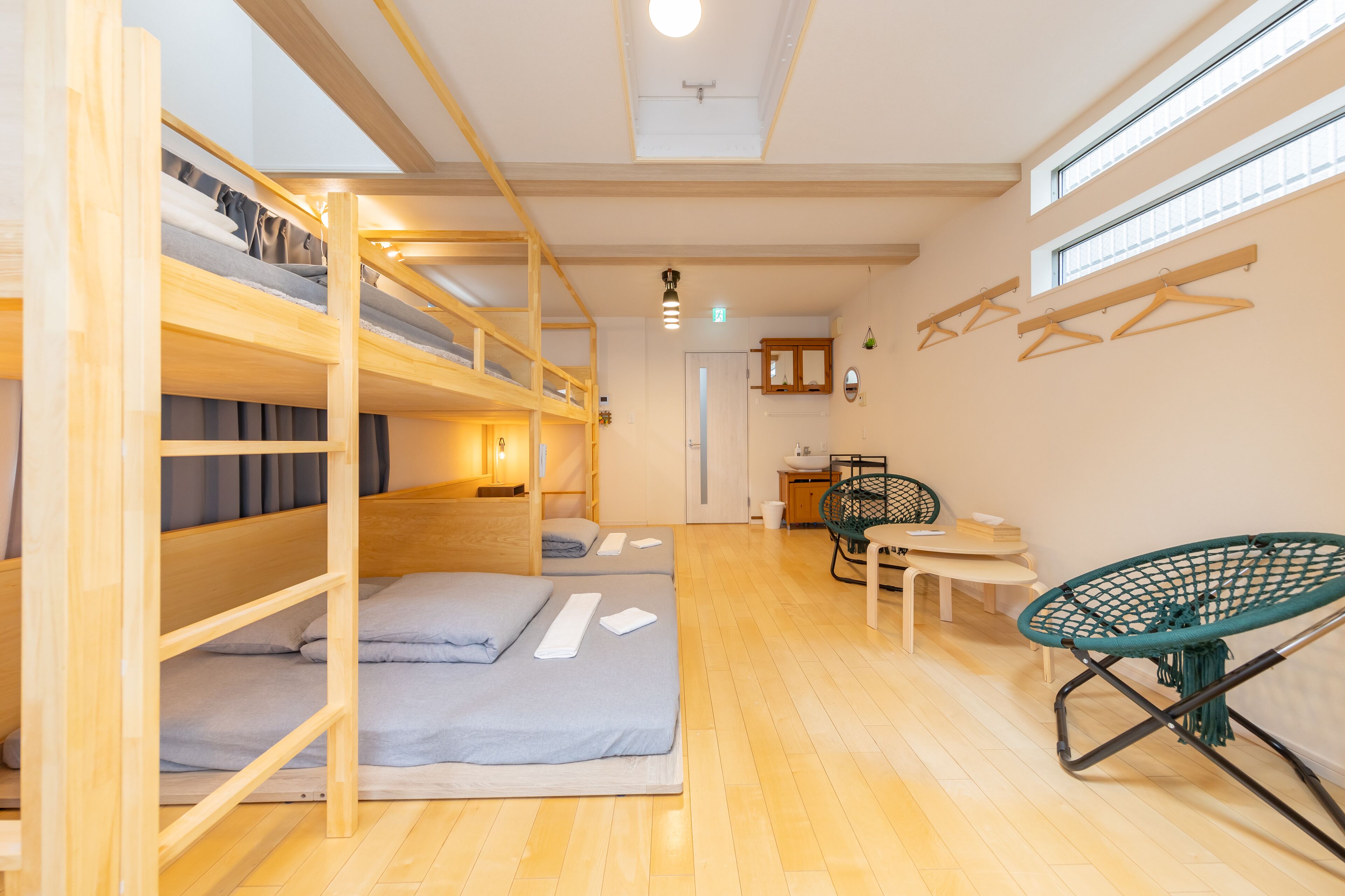 A dormitory room with bunk beds, a desk, a chair, and a window.