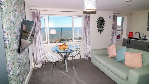 Um quarto com uma mesa de jantar, um sofá, vista para o mar e uma cozinha.