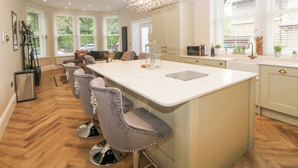 A modern kitchen with a large island, bar stools, and a chandelier. - Cavendish Suite (Buxton)