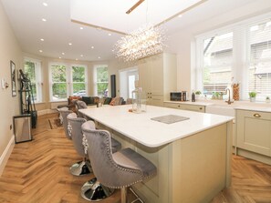 A modern kitchen with a large island, bar stools, and a chandelier. - Cavendish Suite (Buxton)