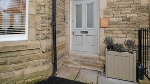 A stone building with a white door marked with the number 16, a small wooden plaque, and a metal gate. - Cavendish Suite (Buxton)