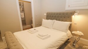 A neatly made bed with white linens, a tufted headboard, and a bedside table with a lamp. - Cavendish Suite (Buxton)