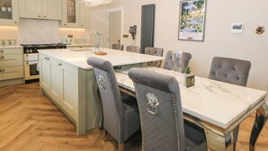 A modern kitchen with a central island, built-in appliances, and a dining area with a marble table and upholstered chairs. - Cavendish Suite (Buxton)