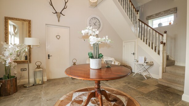 A well-lit foyer with a round wooden table, a clock, a mirror, and a staircase. - The Coach House (Haywards Heath)