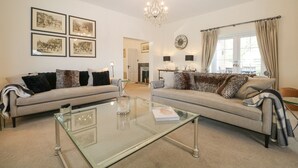 A spacious living room with two sofas, a glass coffee table, and a chandelier. - The Coach House (Haywards Heath)
