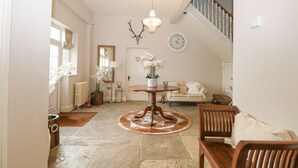 A spacious living area with a round wooden table, a chandelier, a sofa, and a staircase. - The Coach House (Haywards Heath)